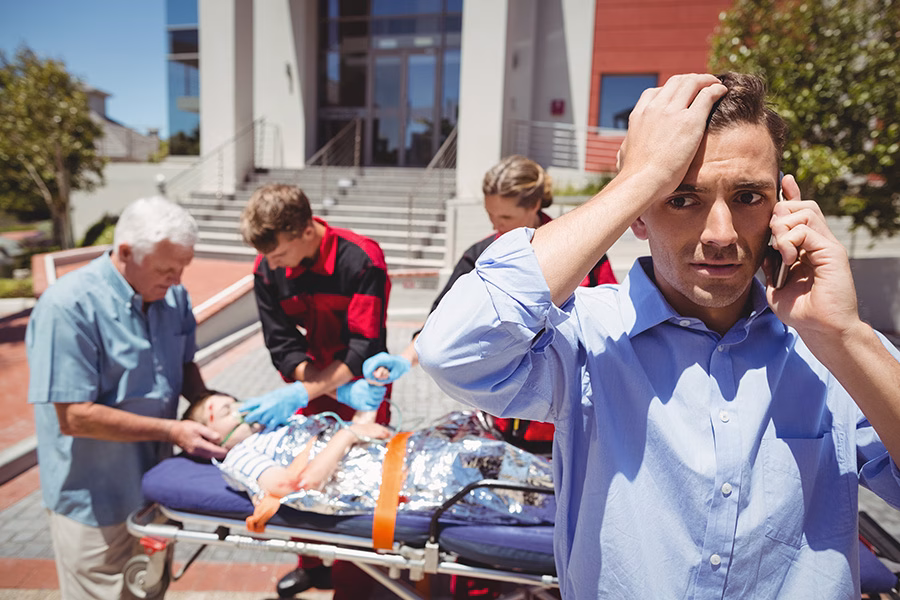 art 4-man-talking-mobile-phone-paramedics-examining-injured-boy-background